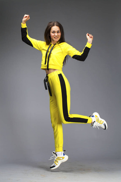 Portrait of a young beautiful brunette woman in yellow tracksuit - Φωτογραφία, εικόνα