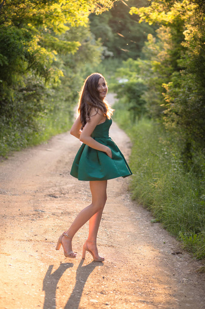 Brunette girl in glamorous green dress and high heels, shoes in nature. - Fotoğraf, Görsel