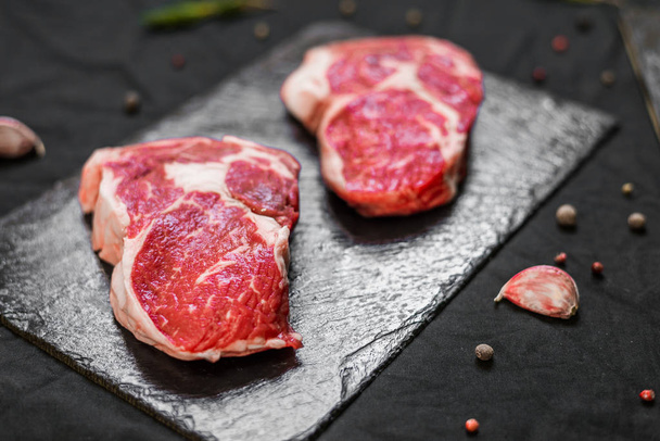 Rib eye beef cow steak meat with spices and herbs against black background - Foto, Imagen
