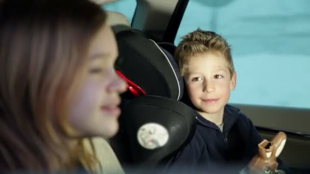 μικρός αδερφός στο πίσω κάθισμα του αυτοκινήτου πειράγματα αδελφή με σοκολάτα κουνέλι - Πλάνα, βίντεο