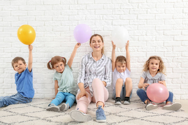 Cute little children with nursery teacher and air balloons sitting near white brick wall - Фото, зображення