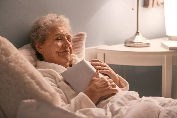 Старша жінка з книгою спить в ліжку вночі
 - Фото, зображення