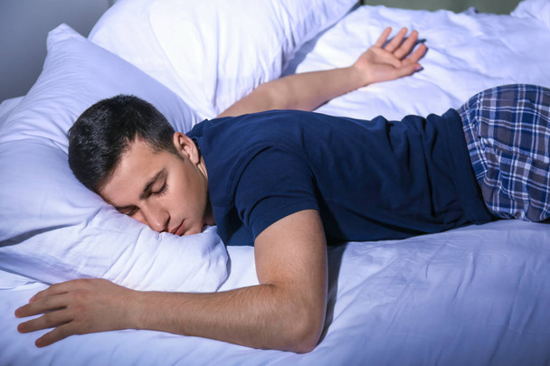 Νεαρός άνδρας που κοιμάται στο κρεβάτι τη νύχτα - Φωτογραφία, εικόνα