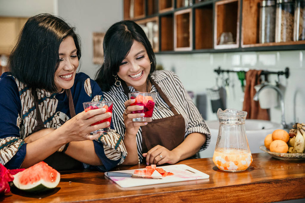 Two asian woman enjoy sweet drink in the kitchen - Photo, image