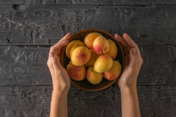 Bowl of apricots in the hands of a child on a wooden table. - Fotografie, Obrázek