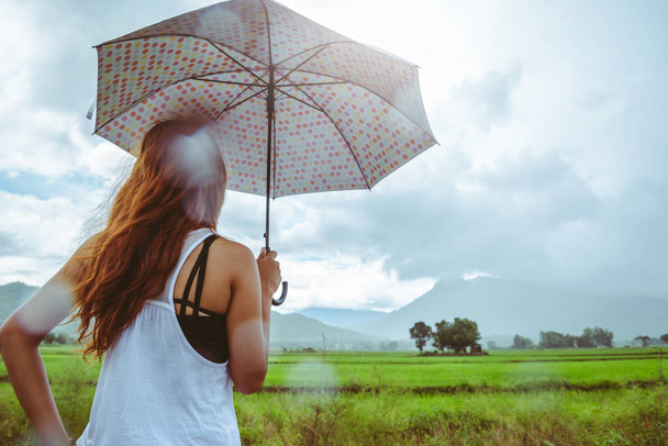 Aziatische vrouwen reizen ontspannen in de vakantie. Vrouwen staan in de regen parasols. Op de weide tijdens het regenseizoen. Thailand - Foto, afbeelding