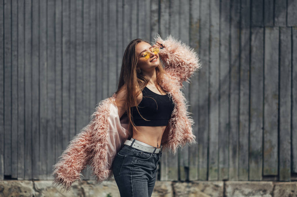 Портрет однієї стильної дівчини в рожевому пальто та сучасних жовтих сонцезахисних окулярах, що позують на вулиці
 - Фото, зображення