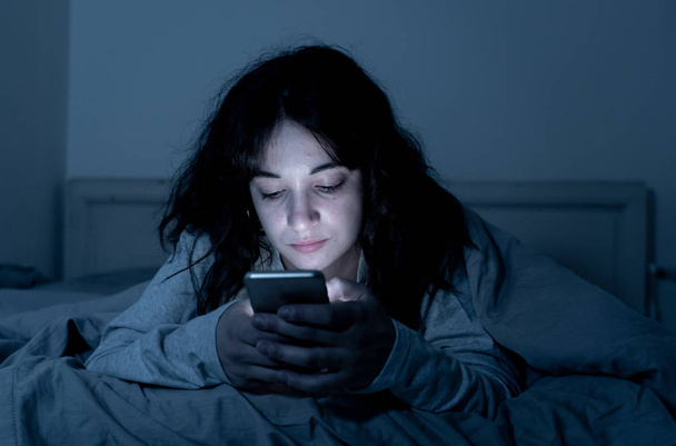 Addicted young woman chatting and surfing on the internet using her smart phone sleepy, bored and tired late at night. Dramatic dark light. In Internet, Mobile addiction and insomnia concept. - Photo, image