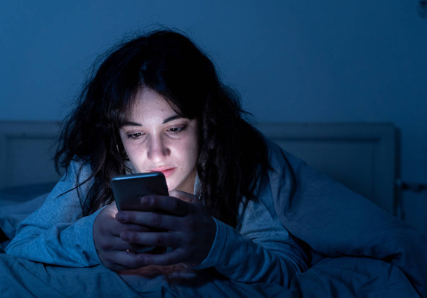 Addicted young woman chatting and surfing on the internet using her smart phone sleepy, bored and tired late at night. Dramatic dark light. In Internet, Mobile addiction and insomnia concept. - Foto, Imagen