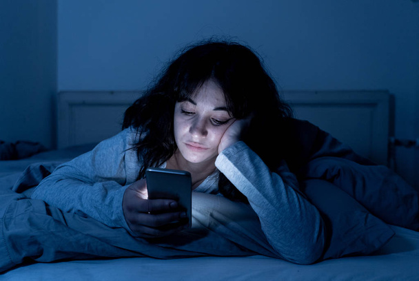 Addicted young woman chatting and surfing on the internet using her smart phone sleepy, bored and tired late at night. Dramatic dark light. In Internet, Mobile addiction and insomnia concept. - Zdjęcie, obraz