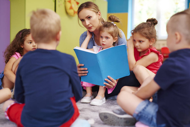 Female teacher is reading a book during classes in preschool  - Photo, Image