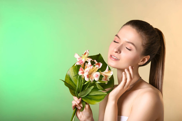 Beautiful young woman with tropical leaf and flowers on color background - Foto, Imagen