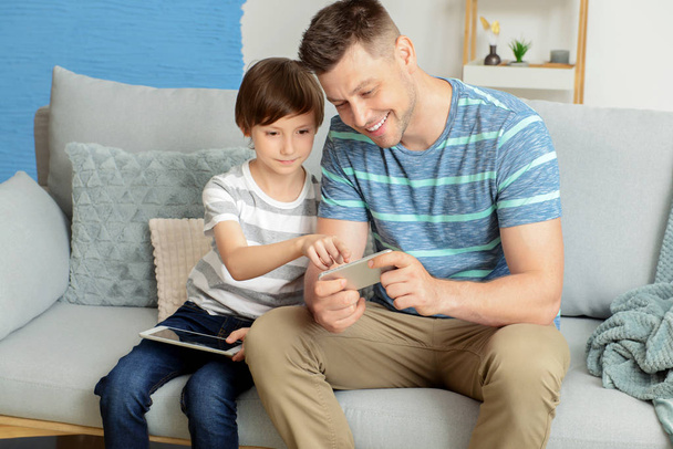 Otec a jeho syn s tabletovým počítačem a mobilním telefonem čas trávení doma - Fotografie, Obrázek