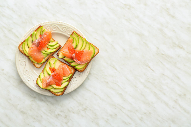 Bord met smakelijke avocado-toast op lichte tafel - Foto, afbeelding