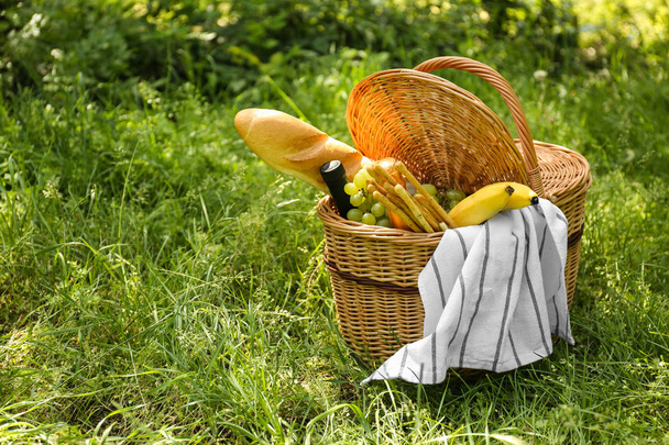 Плетеная корзина с вкусной едой и напитками для романтического пикника в парке
 - Фото, изображение