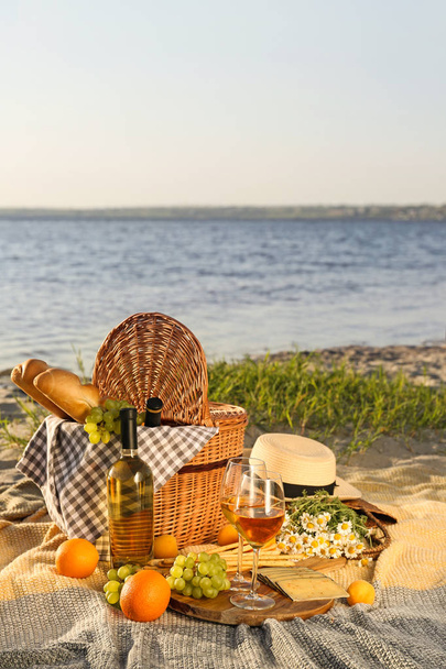 Плетеная корзина с вкусной едой и напитками для романтического пикника у реки
 - Фото, изображение