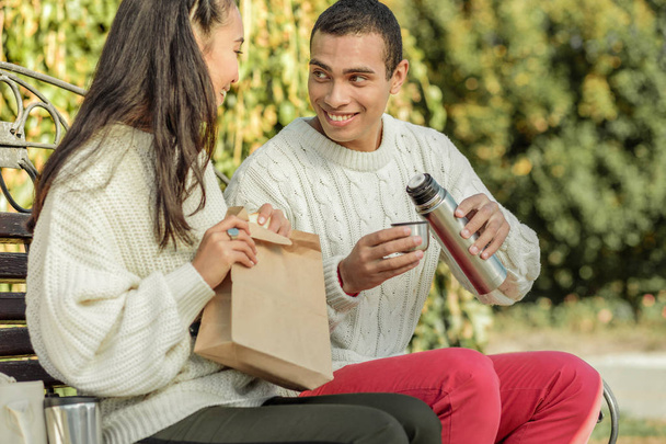 Excited young couple sitting on the bench and having mini picnic - Foto, imagen