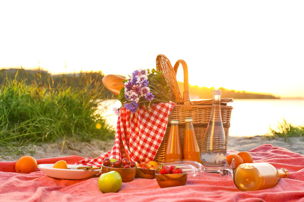 Panier en osier avec nourriture savoureuse et boisson pour un pique-nique romantique près de la rivière
 - Photo, image