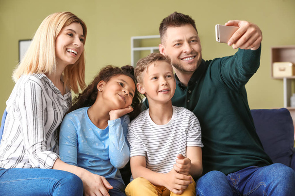 Ευτυχισμένο ζευγάρι με μικρά υιοθετημένα παιδιά που βγάζουν selfie στο σπίτι - Φωτογραφία, εικόνα