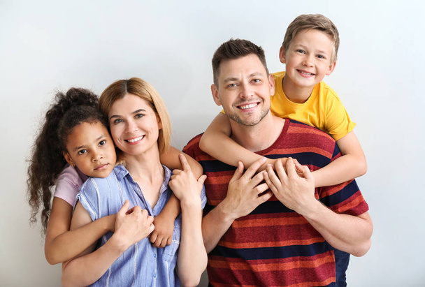 Happy couple with little adopted children on light background - Photo, Image