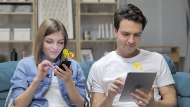 Mladý pár používající smartphone a tablet, létající smajlíky, Emojis a líbí - Záběry, video