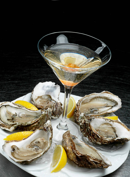 Oysters plate with lemon on dark background. Oyster dinner with champagne in restaurant. Oysters with lemon and a glass of alcohol - Photo, Image