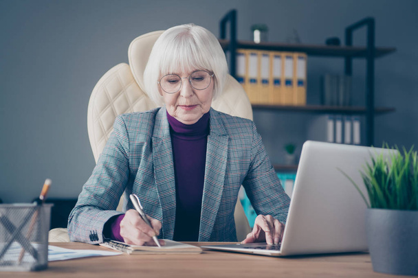 Closeup photo of aged business lady noting webinar report details chief organization sit chair notebook table wear specs costume jacket - Valokuva, kuva