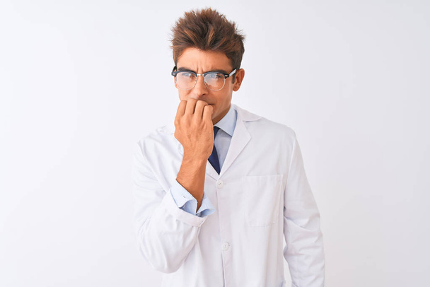 Jonge knappe sciencist man het dragen van een bril en vacht over geïsoleerde witte achtergrond op zoek gestrest en nerveus met handen op mond bijten nagels. Angst probleem. - Foto, afbeelding