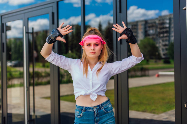 Portrait of an emotional girl in a pink cap visor and protective gloves for rollerblades and skateboarding. - Foto, afbeelding