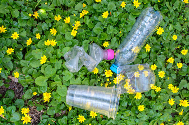 garrafas de plástico descartado e embalagem na grama com flores amarelas
 - Foto, Imagem