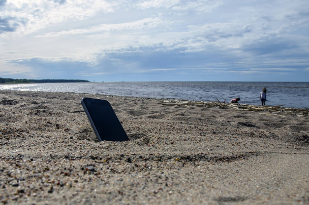mobile phone lying on the beach in the sand. weatherproof phones, lost phone concept, data loss. - Foto, afbeelding