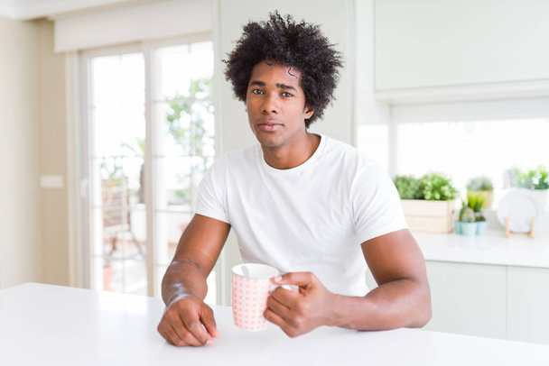 Afro-Américain aux cheveux afro boire une tasse de café avec une expression confiante sur le visage intelligent penser sérieux
 - Photo, image