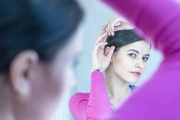 Young woman touching her face with hands , standing in bathroom, reflecting in mirror. Daily skin treatment concept - Foto, Imagen