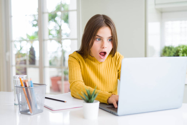 Beautiful young girl studying for school using computer laptop scared in shock with a surprise face, afraid and excited with fear expression - Фото, изображение
