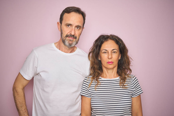 Beautiful middle age couple together standing over isolated pink background with serious expression on face. Simple and natural looking at the camera. - Foto, Bild