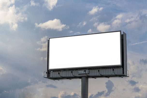 Cartellone con sfondo bianco per testo e immagini con pubblicità in piedi su un palo, sullo sfondo di nuvole potenti e belle
. - Foto, immagini