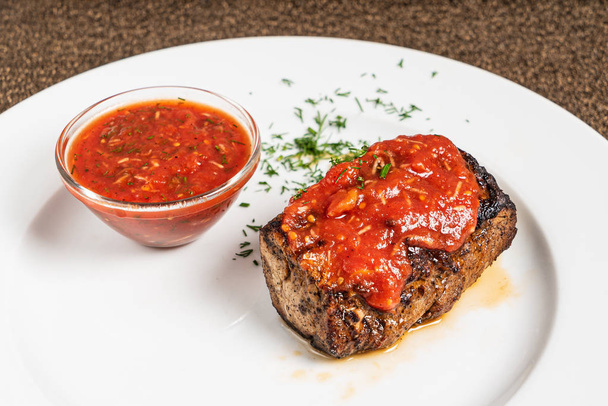 steak with tomato sauce on white plate - Фото, изображение