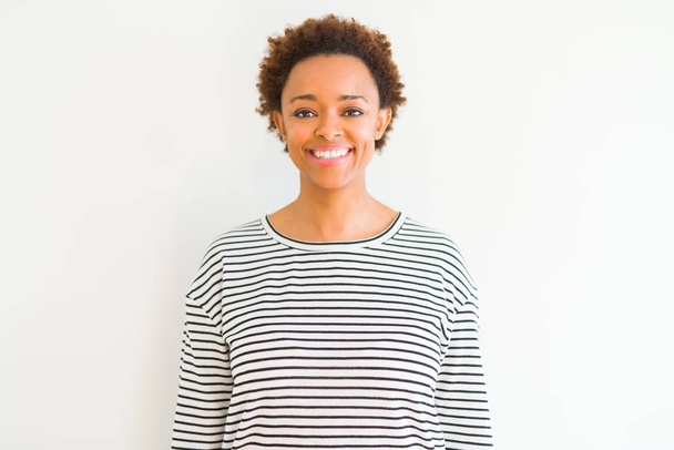 Νέα όμορφη αφρικανική Αμερικανίδα γυναίκα φορώντας ρίγες πουλόβερ πάνω από το λευκό φόντο με ένα χαρούμενο και δροσερό χαμόγελο στο πρόσωπο. Τυχερός άνθρωπος. - Φωτογραφία, εικόνα