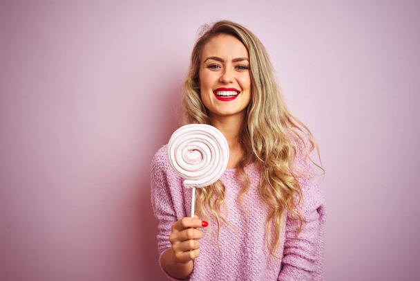 Młoda piękna kobieta jedząca słodki cukierek nad różowym białym tle z szczęśliwą twarzą i uśmiechając się z pewnym uśmiechem, pokazując zęby - Zdjęcie, obraz