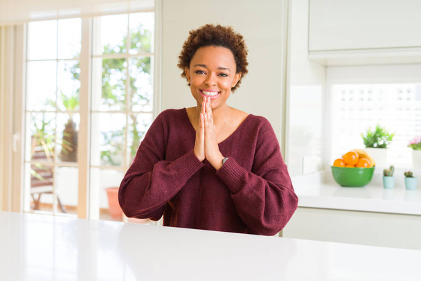 Giovane bella donna afroamericana a casa a pregare con le mani insieme chiedendo perdono sorridente fiducioso
. - Foto, immagini