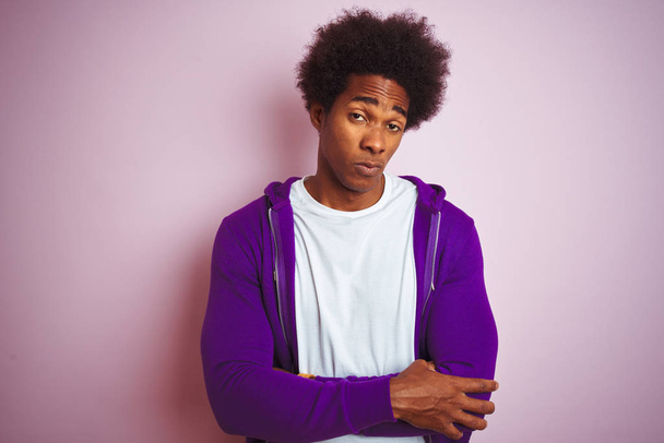 孤立したピンクの背景に立つ紫色のスウェットシャツを着た若いアフリカ系アメリカ人男性は懐疑的で神経質で、腕を組んだ顔に失望した表情をしている。否定的な人. - 写真・画像