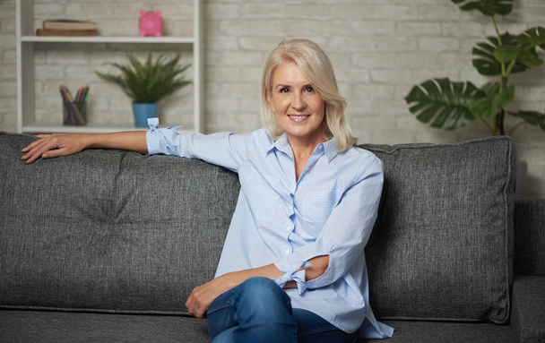 Pretty middle aged woman is sitting on a sofa at home - Fotoğraf, Görsel
