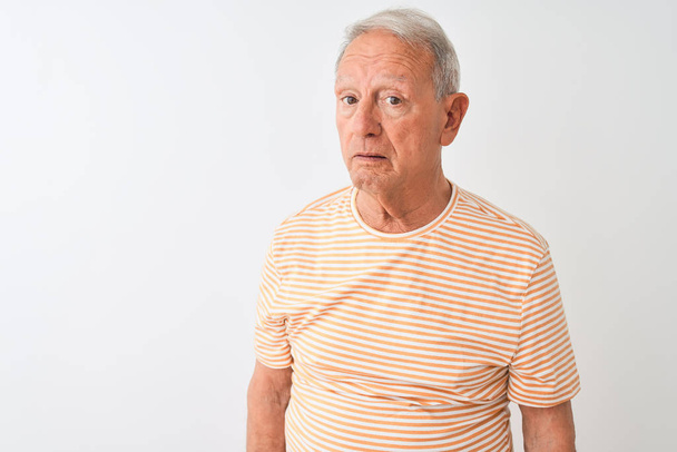 Homme âgé aux cheveux gris portant un t-shirt rayé debout sur un fond blanc isolé, somnolent et fatigué, épuisé par la fatigue et la gueule de bois, les yeux paresseux le matin
. - Photo, image