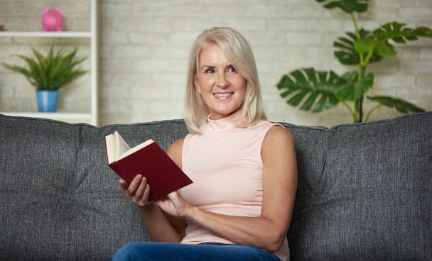 Happy middle aged woman is reading a book at home - Fotoğraf, Görsel