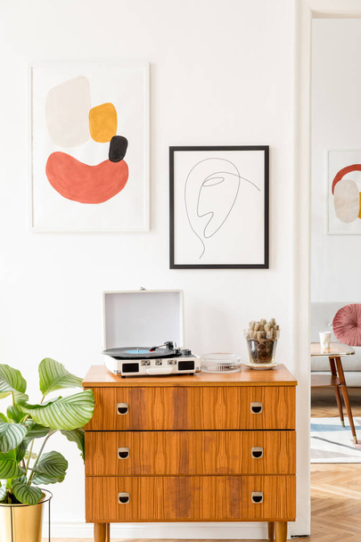 Vintage and retro living room with design commode, vinyl recorder and mock up posters frames on the white walls. Minimalistic room with brown wooden parquet and plants. - 写真・画像