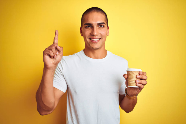 Nuori komea mies juo ottaa pois lasin kahvia keltainen eristetty tausta yllättynyt ajatus tai kysymys sormella onnellinen kasvot, numero yksi
 - Valokuva, kuva