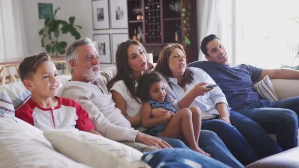 Three generation Hispanic family sitting on the sofa watching TV, grandmother using remote control - Footage, Video