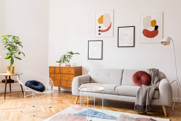 Stylish vintage decor in a spacious flat interior with design grey sofa, armchair, retro commode and posters on the wall. Brwon wooden parquet, stylish carpet and plants. Bright living room. - Foto, Imagem