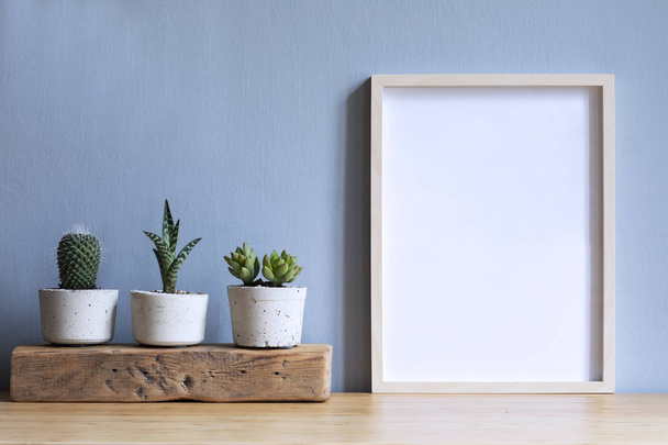 Minimalistic room interior with mock up photo frame on the brown wooden table with beautiful cacti in design hipster cement pot. Grey walls. Stylish and floral concept of mock up poster frame.  - Fotografie, Obrázek