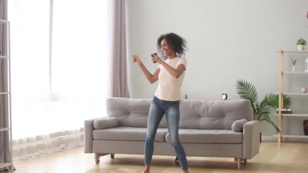 Afrykańska kobieta trzyma smartfon taniec słuchania muzyki w domu - Materiał filmowy, wideo